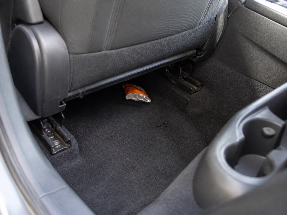Illustrated car footwell inspection scene with a torn snack packet and ambiguous pellets